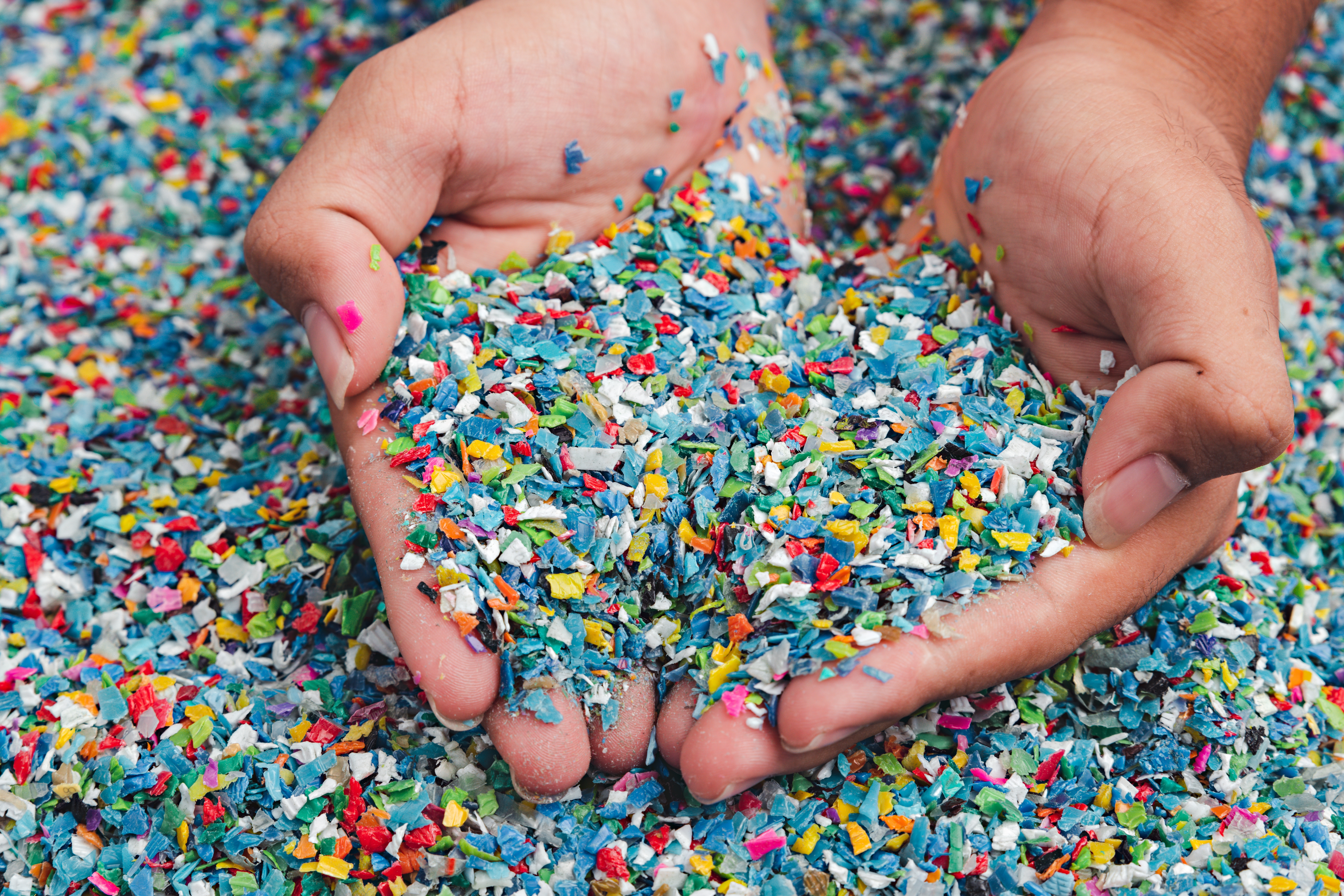Hands holding colorful shredded plastic flakes for recycling and reuse in new plastic products.